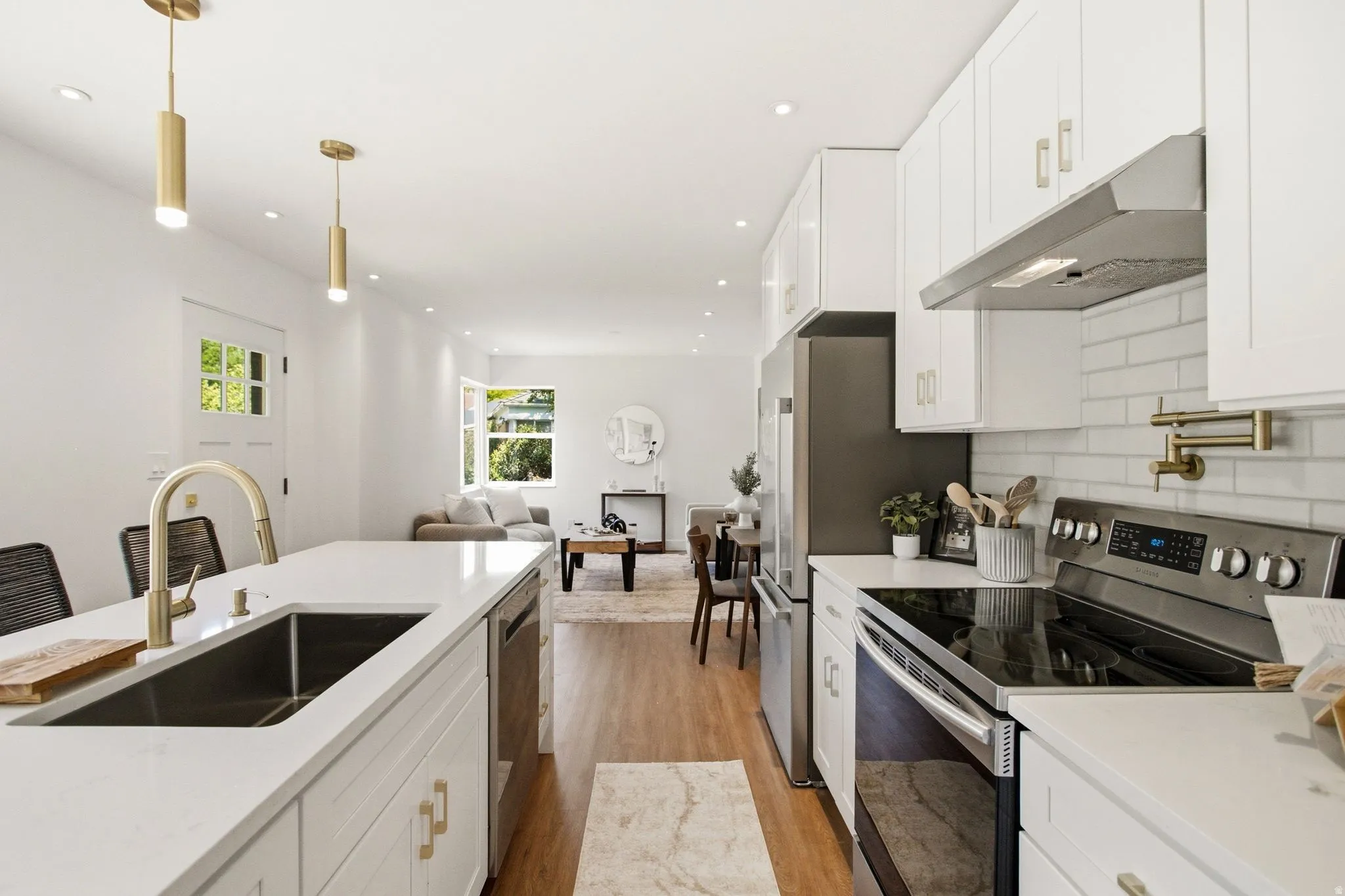 Modern kitchen featuring white cabinetry, stainless steel appliances, a white subway tile backsplash, and a gold-finish pull-down faucet