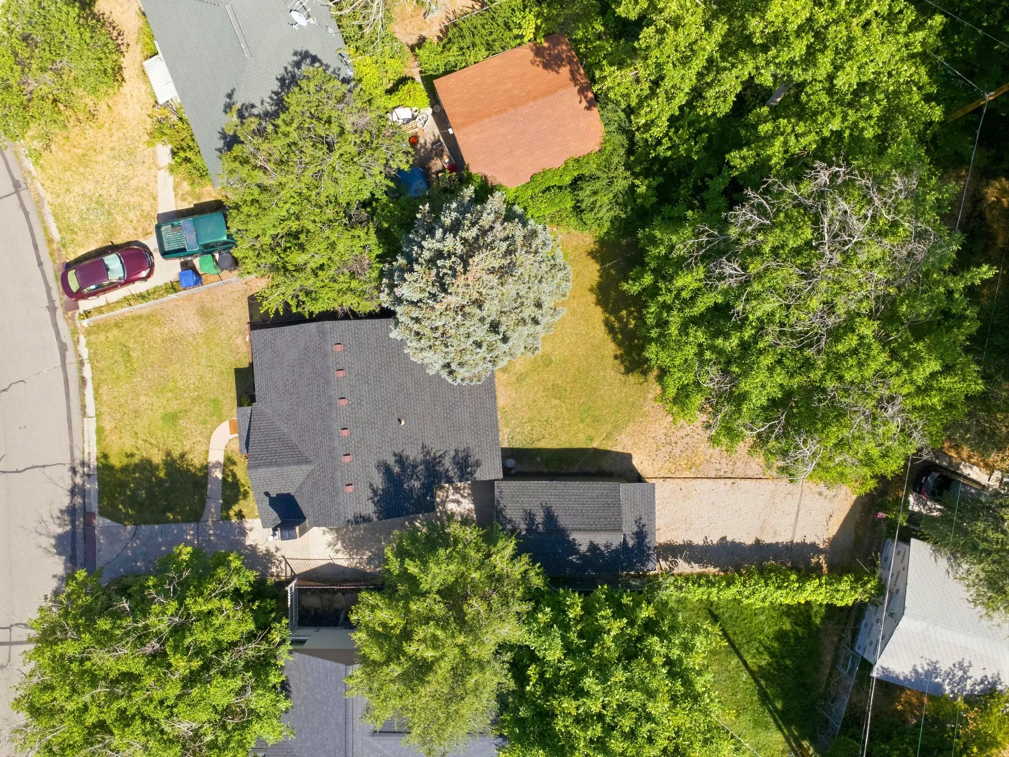 Property featuring a dark shingle roof, mature trees, and a gravel driveway
