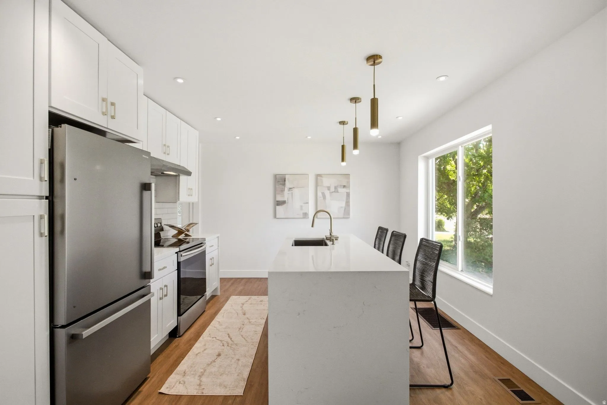 Modern kitchen featuring white cabinetry with brushed brass hardware, stainless steel appliances including a French-door refrigerator and slide-in range, white quartz waterfall island countertop, pendant lighting with brass accents, wood-finish flooring,