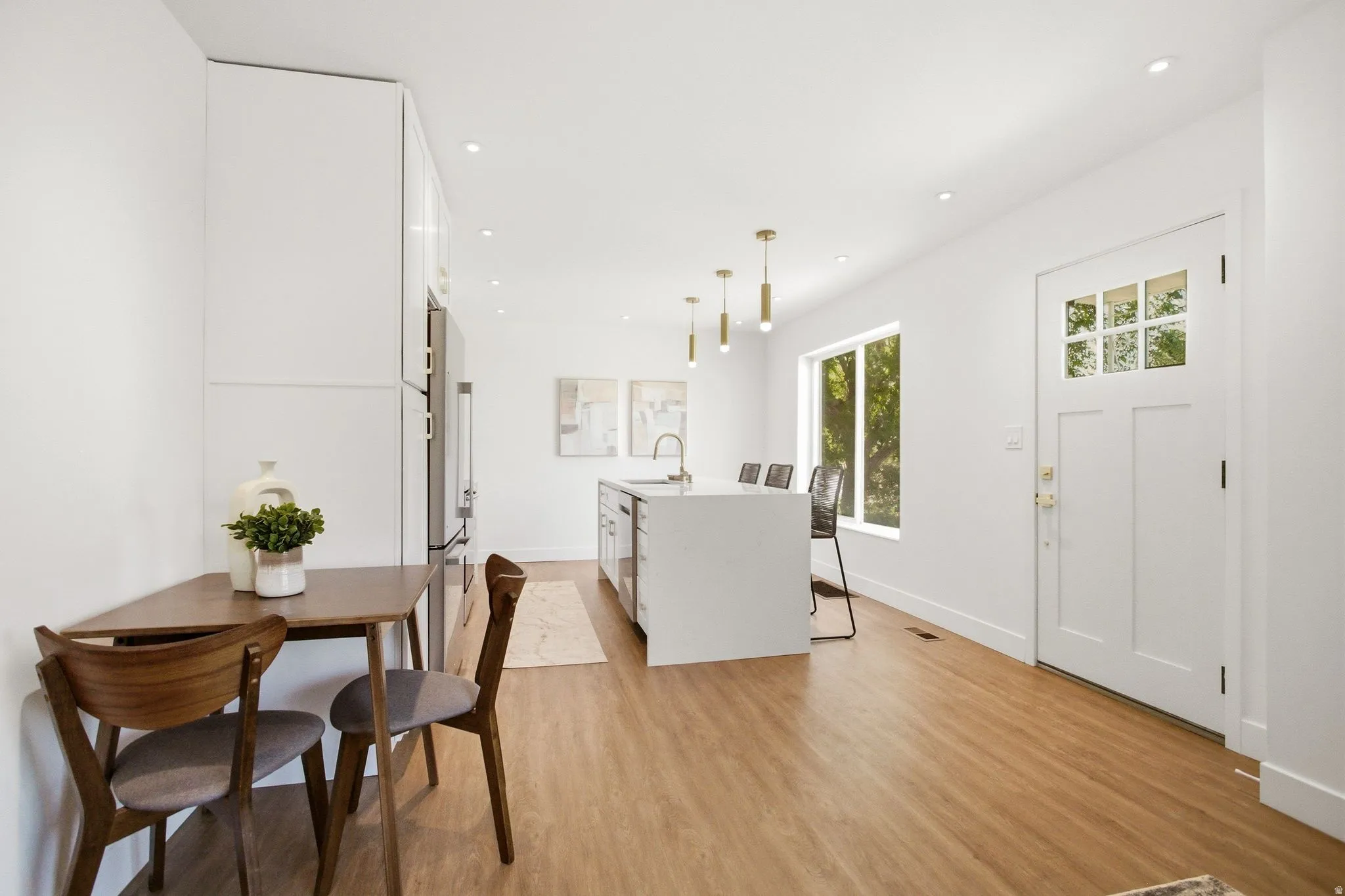 Open-concept living space featuring wood-finish flooring, recessed lighting, and a white kitchen island with a sink and pendant lighting