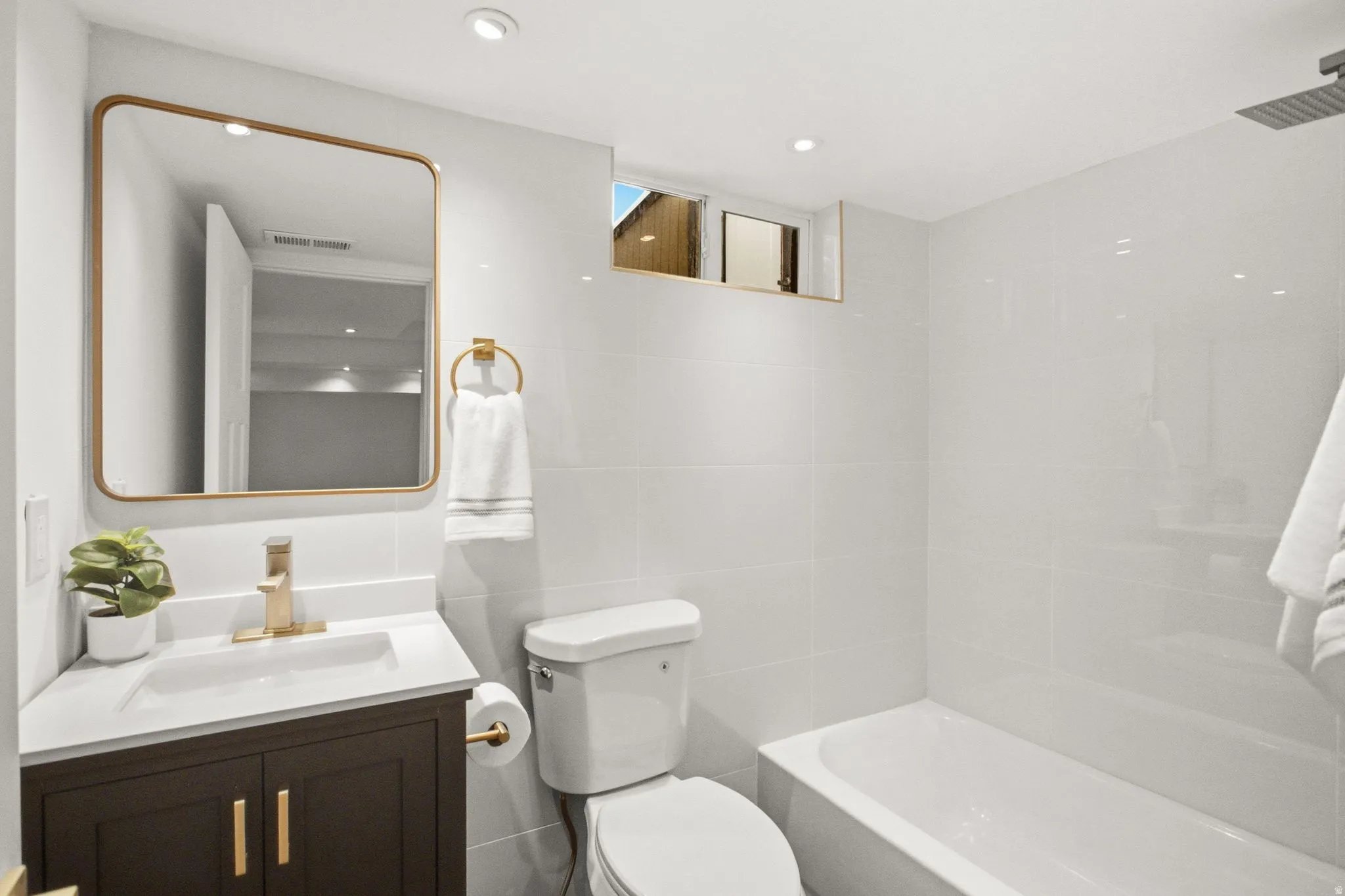 Modern bathroom featuring a dark wood vanity with brass hardware, white quartz countertop, and integrated rectangular sink