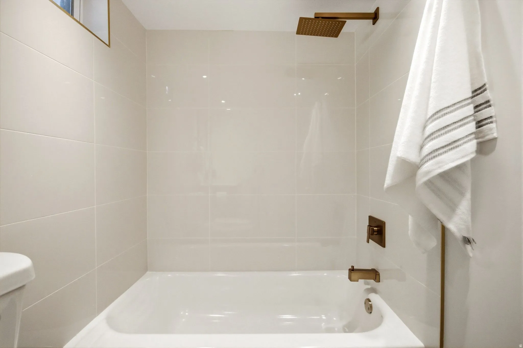 Clean, bright bathroom featuring a white porcelain soaking tub with chrome fixtures, frameless glass shower enclosure, crisp white subway tile walls, recessed ceiling lighting, brushed bronze hardware accents, and a coordinating towel bar with plush white