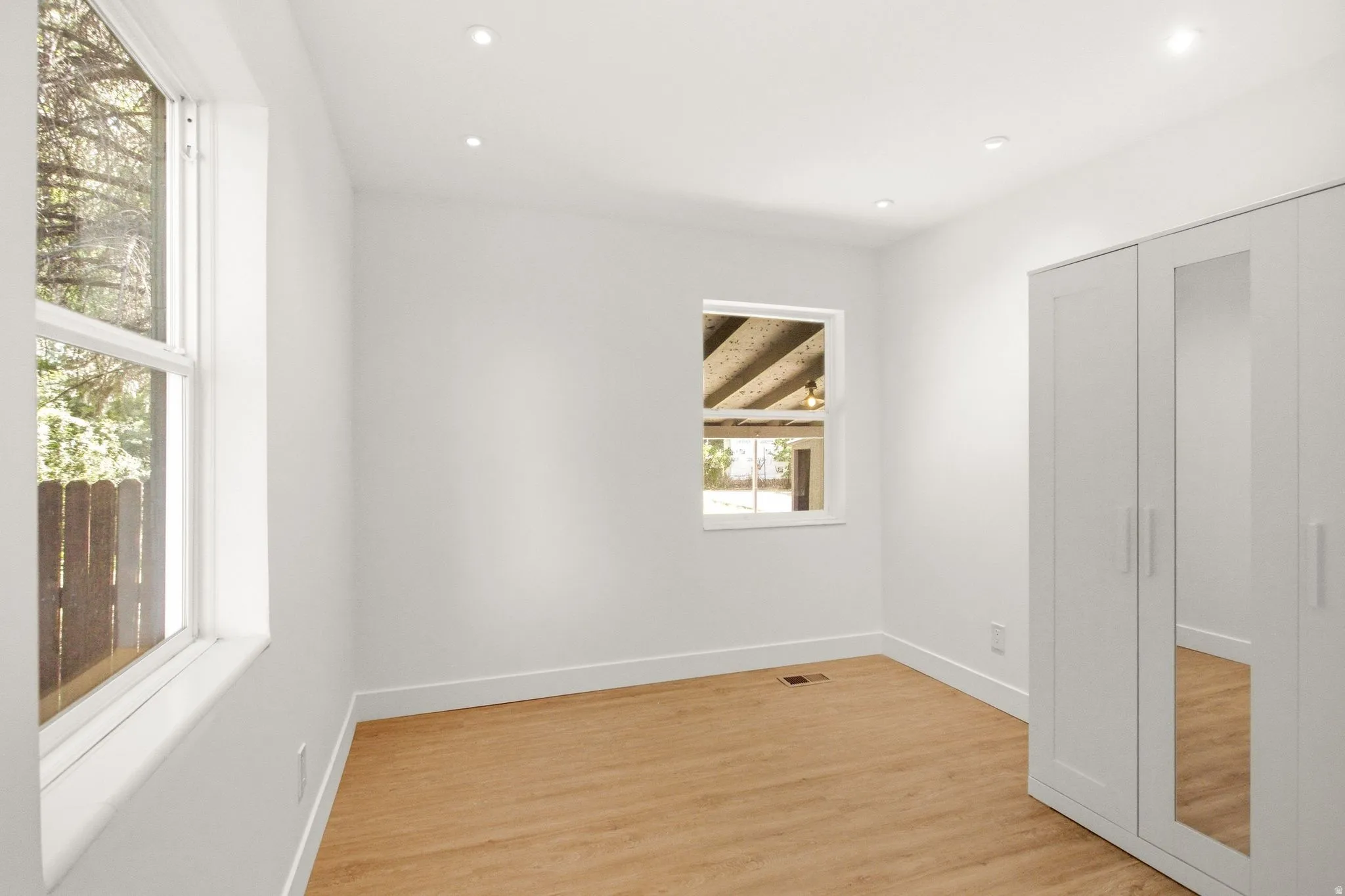 Bright and airy bedroom featuring pristine white walls, recessed ceiling lighting, and refinished wood-finish flooring