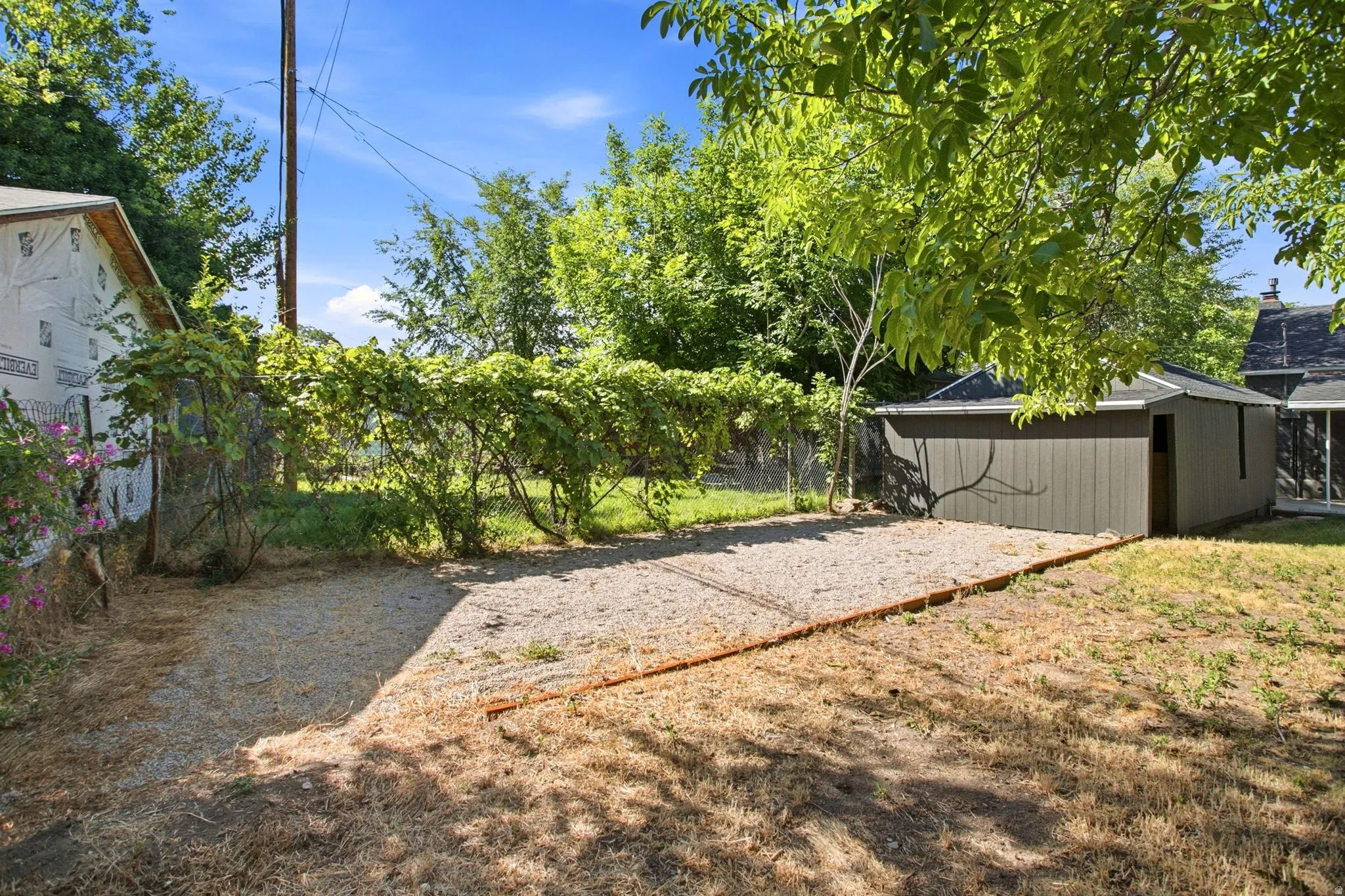 Spacious backyard with mature shade trees, gravel pathways, and detached storage structures