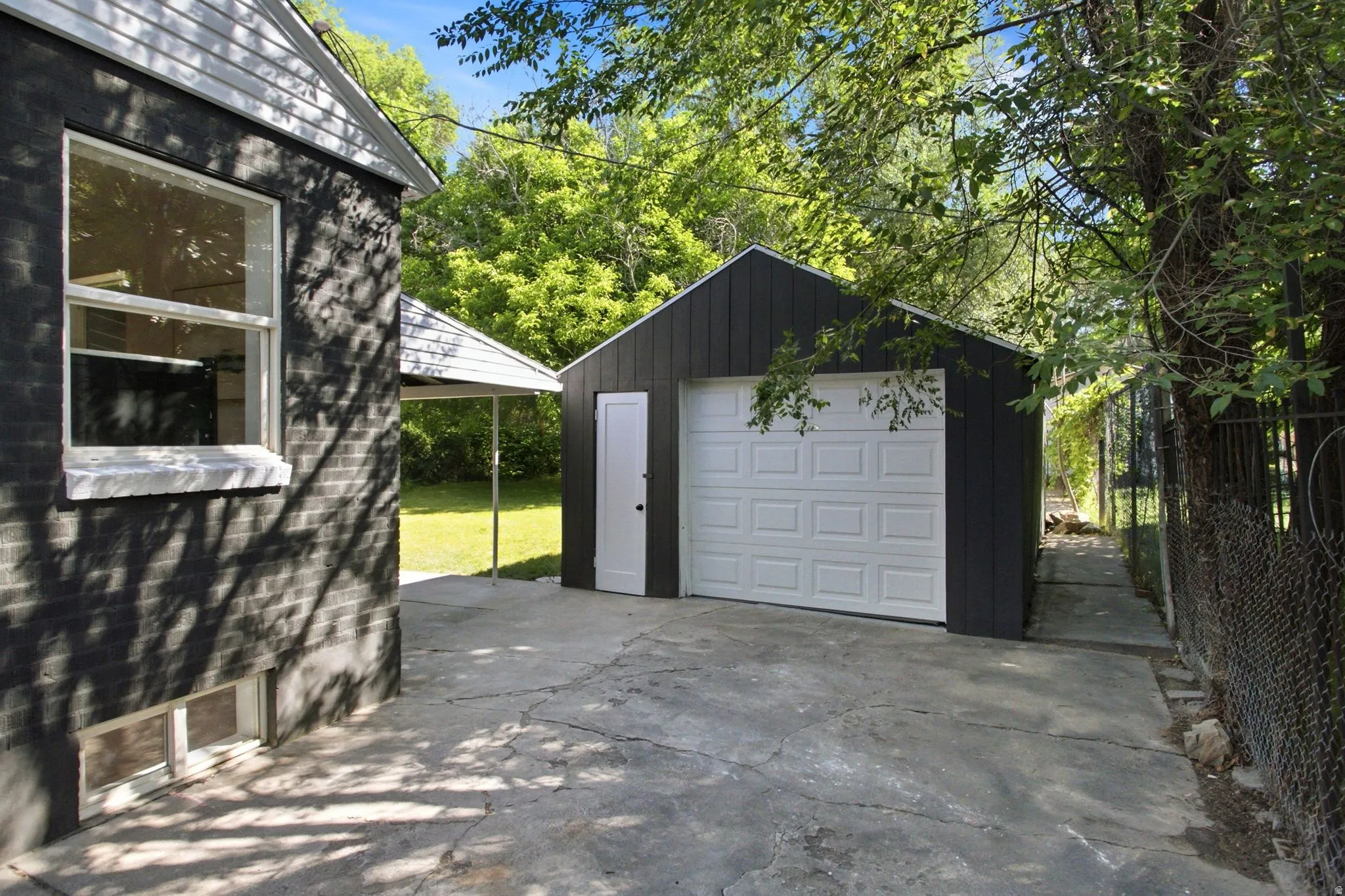 Modern detached garage featuring a white paneled overhead door, black exterior siding, and concrete apron
