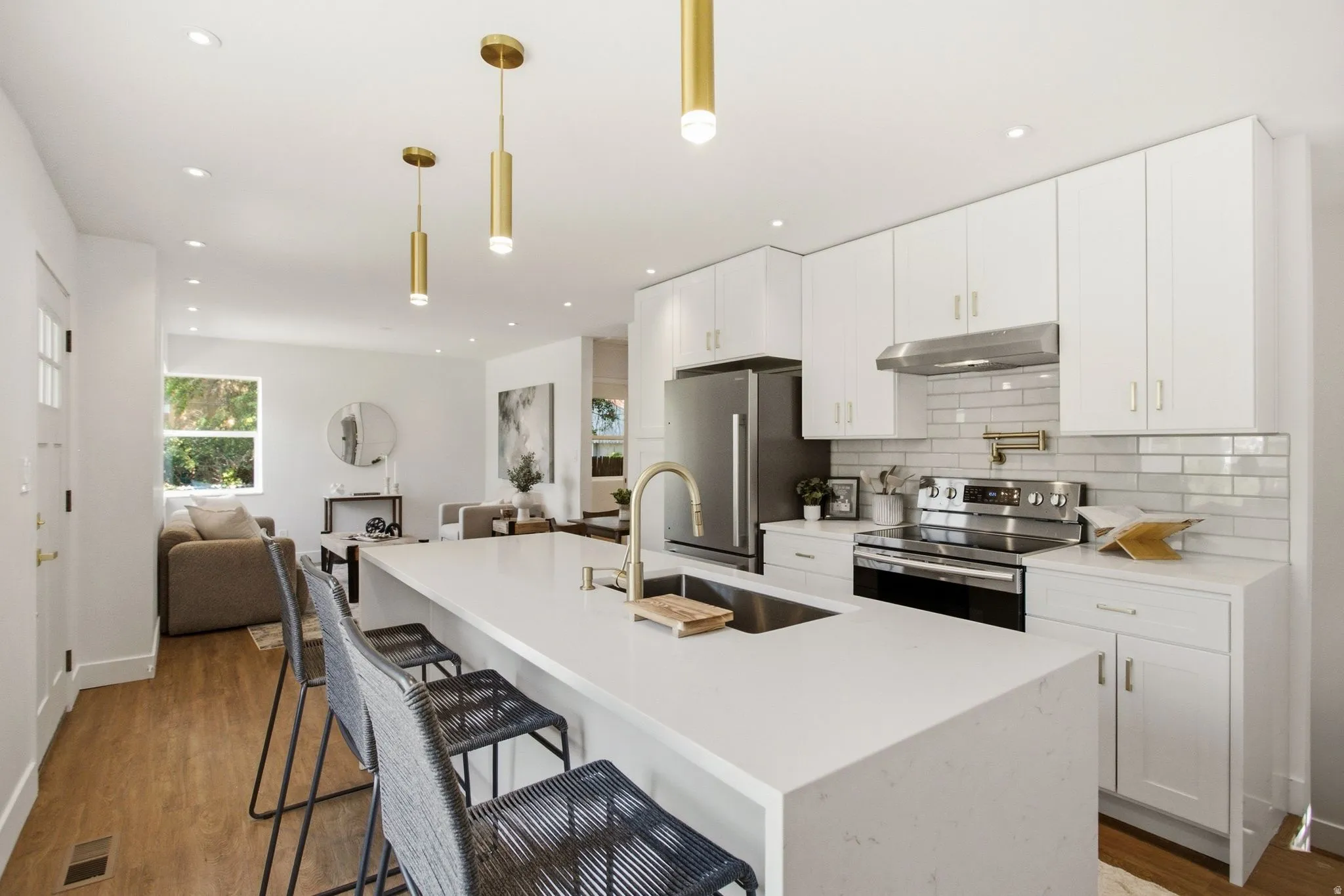 Contemporary kitchen featuring white cabinetry, a large waterfall-edge quartz island with seating for multiple, stainless steel appliances including a gas range and under-counter refrigeration, subway tile backsplash, and pendant lighting
