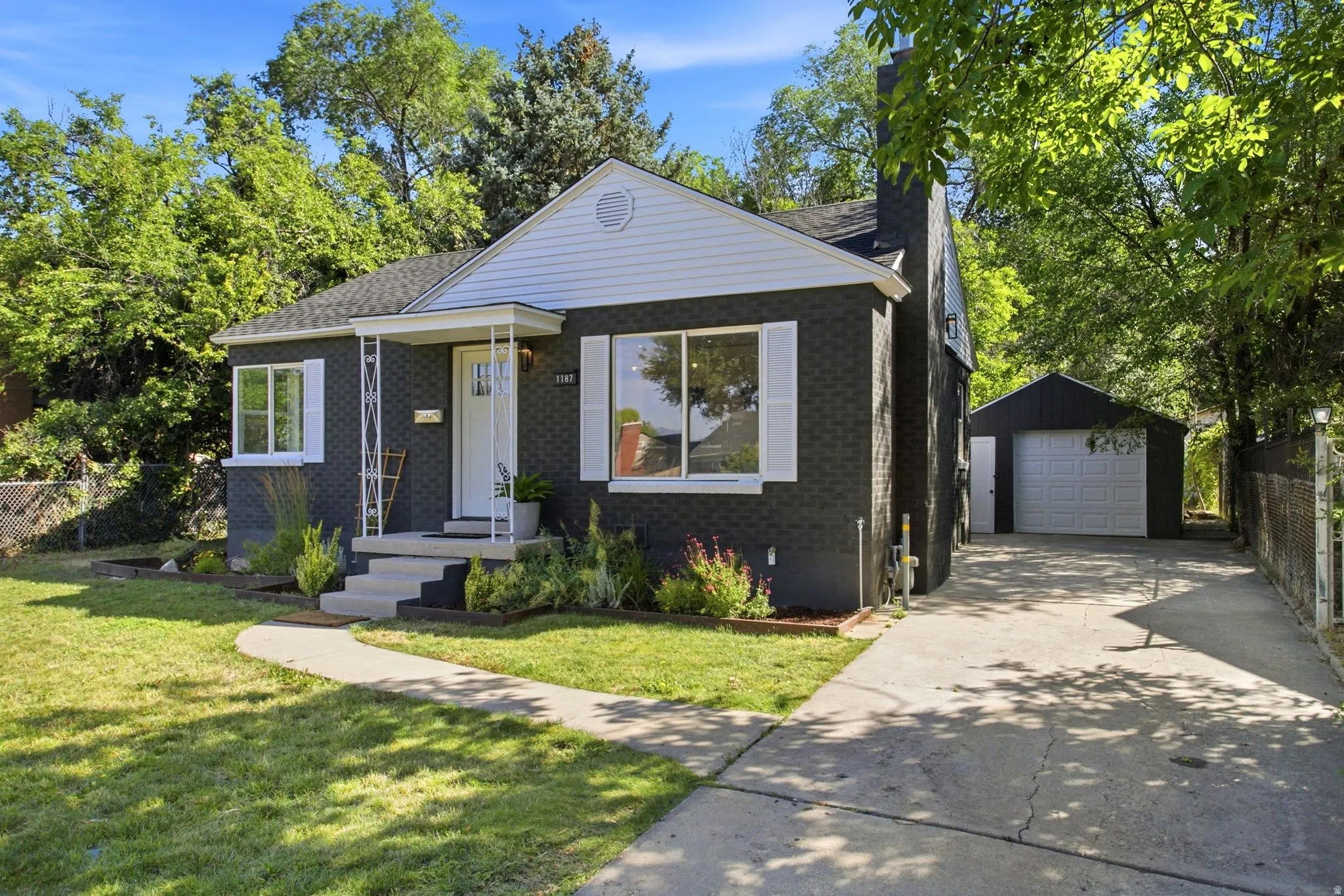 Charcoal brick exterior with white trim and shutters, featuring a covered front entry, a concrete driveway, and a detached garage