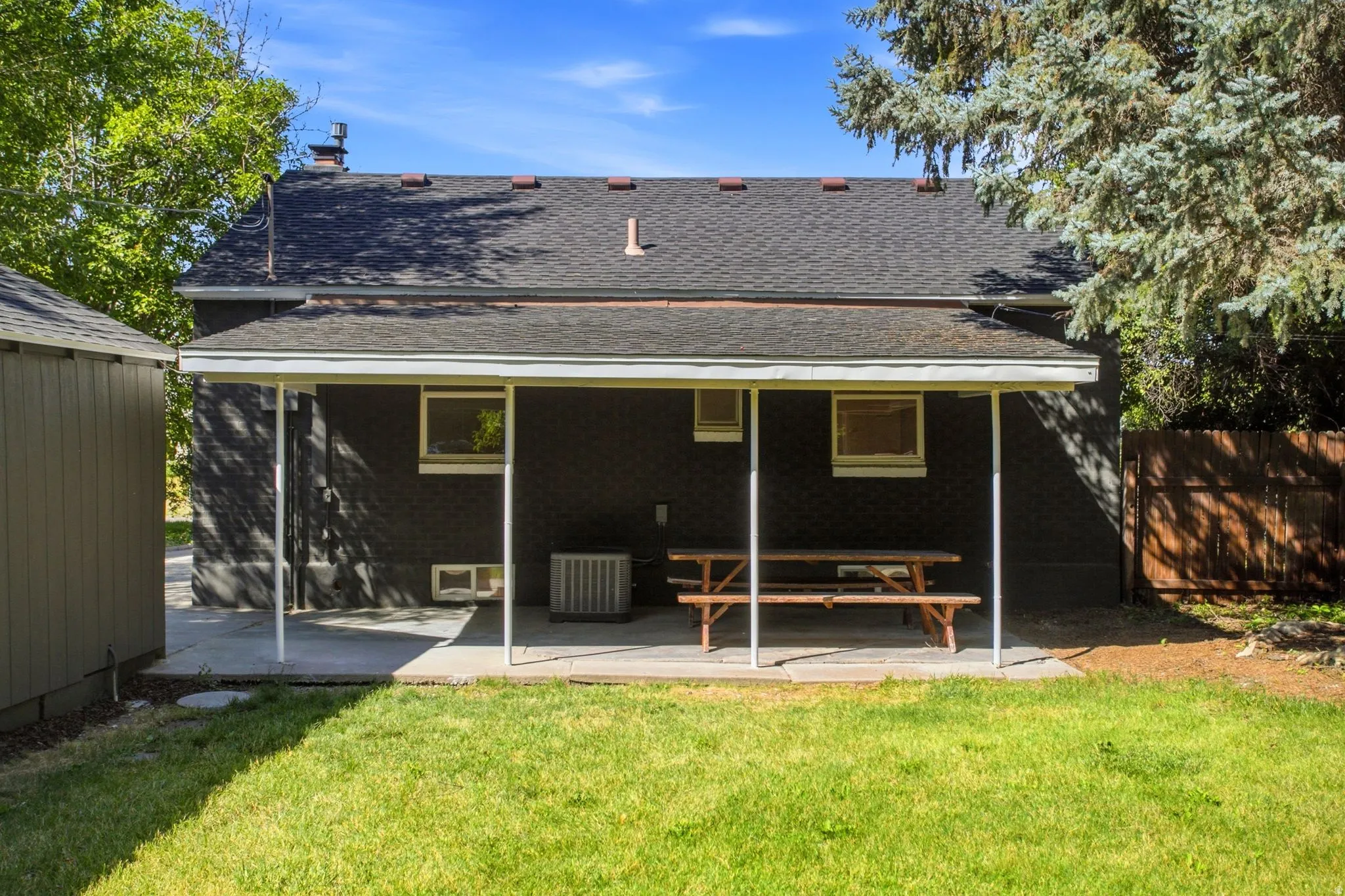 Rear exterior featuring a covered concrete patio, dark-painted brick siding, and a gabled roof
