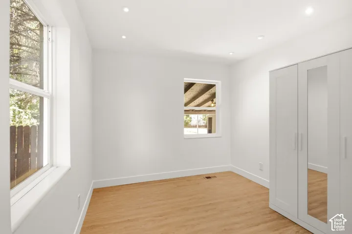 Bright and airy bedroom featuring pristine white walls, recessed ceiling lighting, and refinished wood-finish flooring