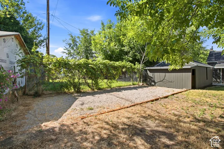 Spacious backyard with mature shade trees, gravel pathways, and detached storage structures