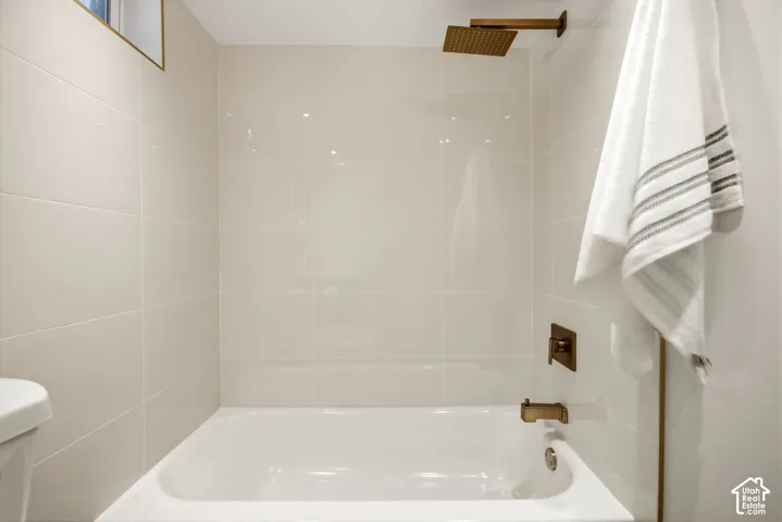Clean, bright bathroom featuring a white porcelain soaking tub with chrome fixtures, frameless glass shower enclosure, crisp white subway tile walls, recessed ceiling lighting, brushed bronze hardware accents, and a coordinating towel bar with plush white