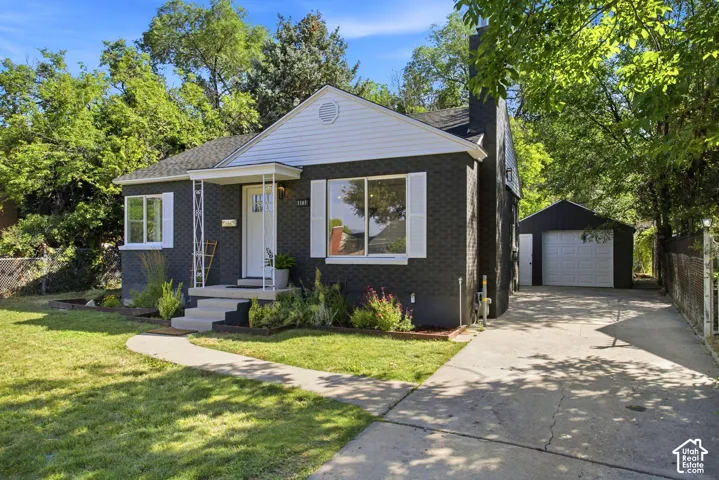 Charcoal brick exterior with white trim and shutters, featuring a covered front entry, a concrete driveway, and a detached garage