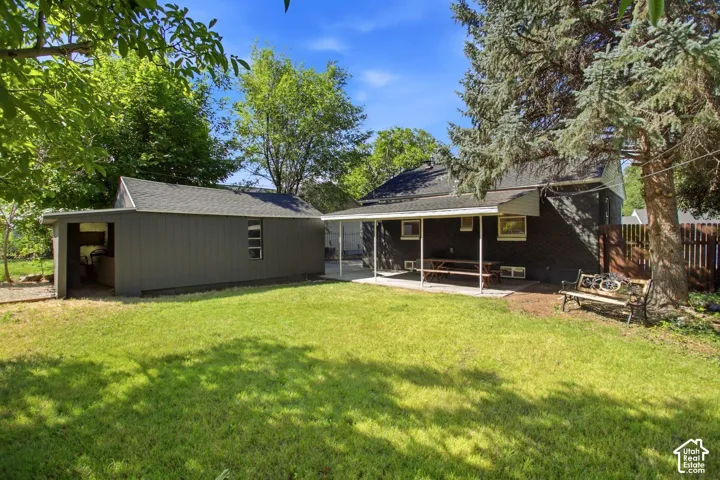 Spacious backyard featuring a manicured lawn, dedicated storage shed, covered patio area, and mature trees