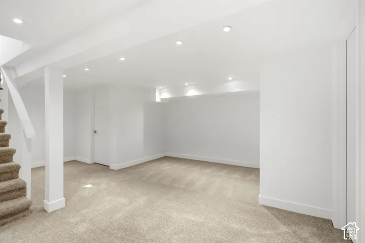 Finished basement featuring open layout with neutral carpet flooring, recessed ceiling lighting, white drywall construction, and structural support columns