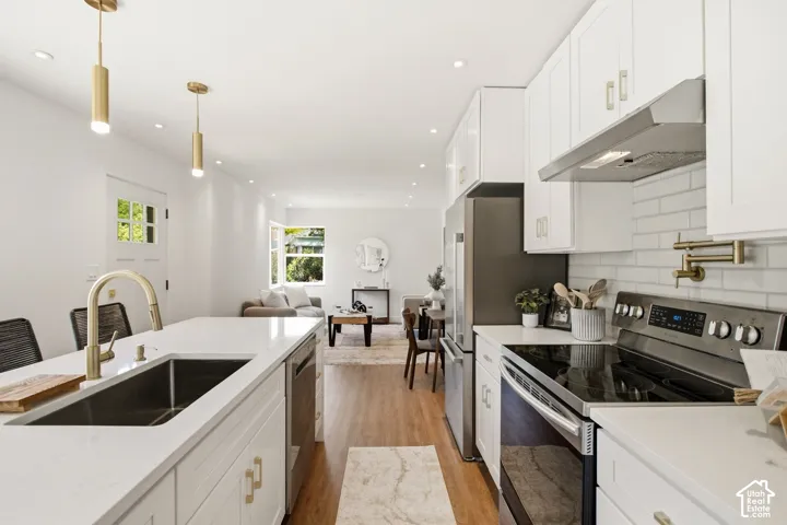 Modern kitchen featuring white cabinetry, stainless steel appliances, a white subway tile backsplash, and a gold-finish pull-down faucet