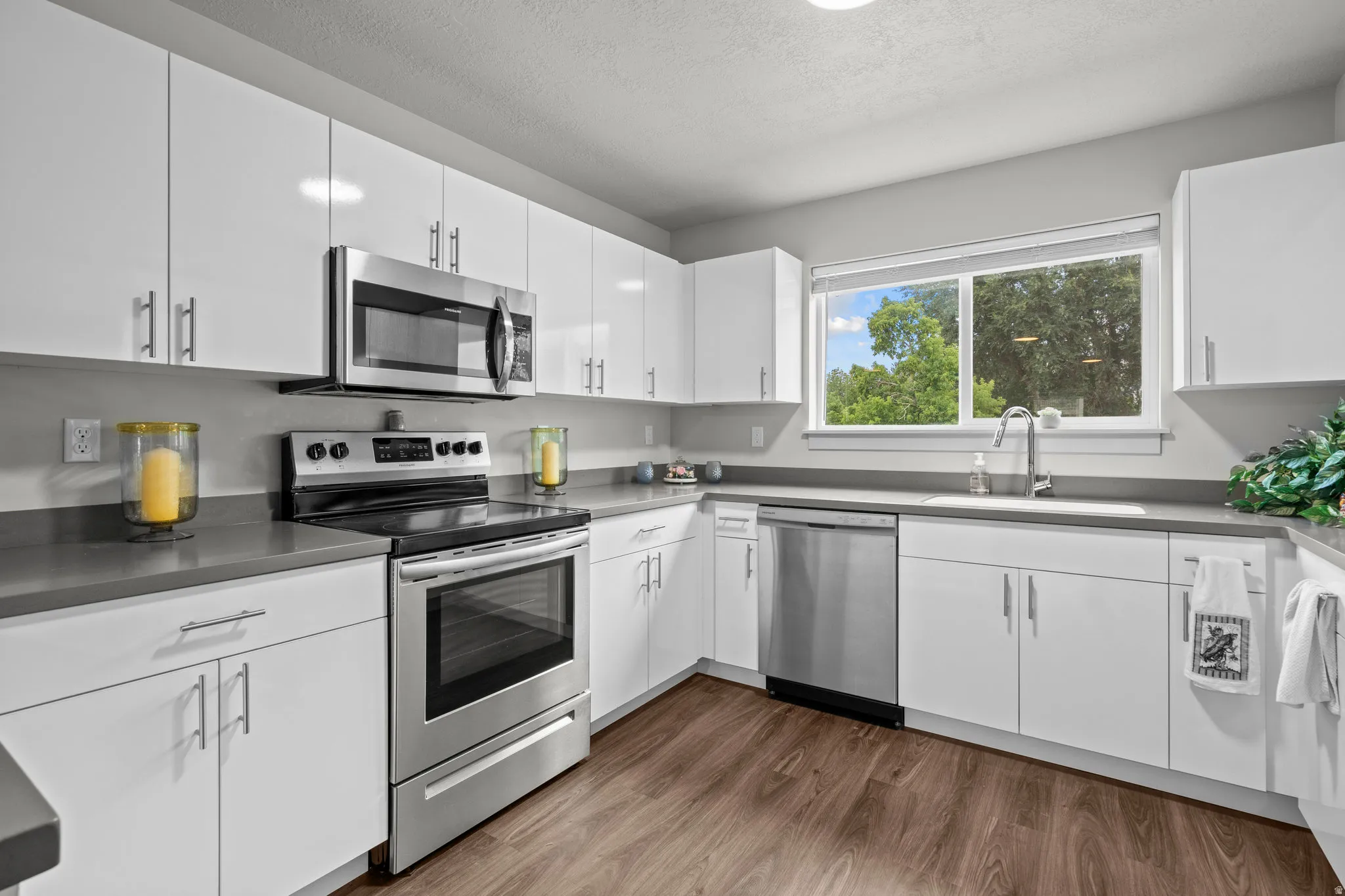Kitchen featuring white cabinetry, stainless steel appliances, grey countertops, and wood-finish flooring