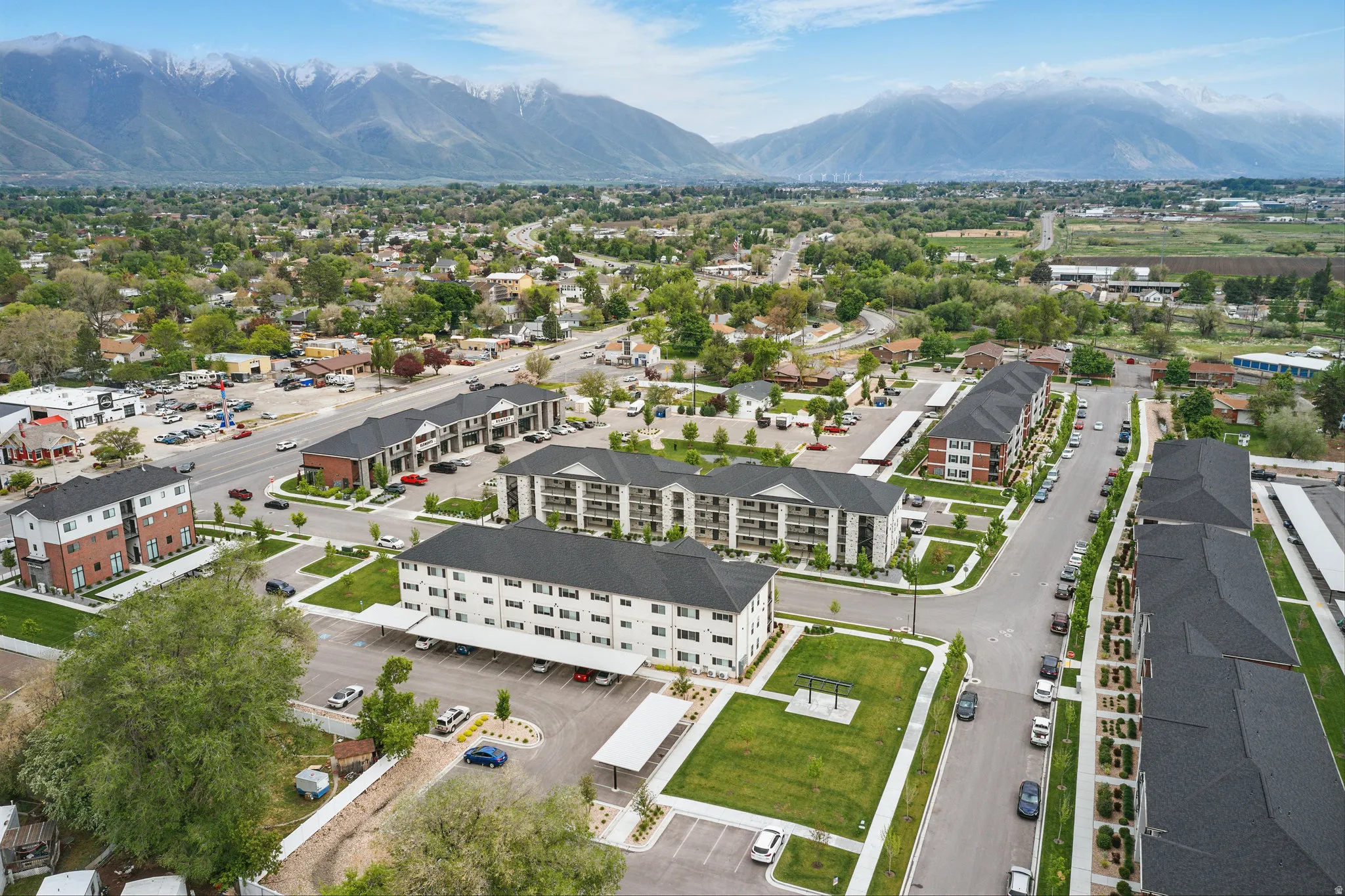 Modern multi-unit residential development featuring contemporary architecture with clean linear forms, integrated landscaping with mature greenery, dedicated parking areas, and mountain backdrop