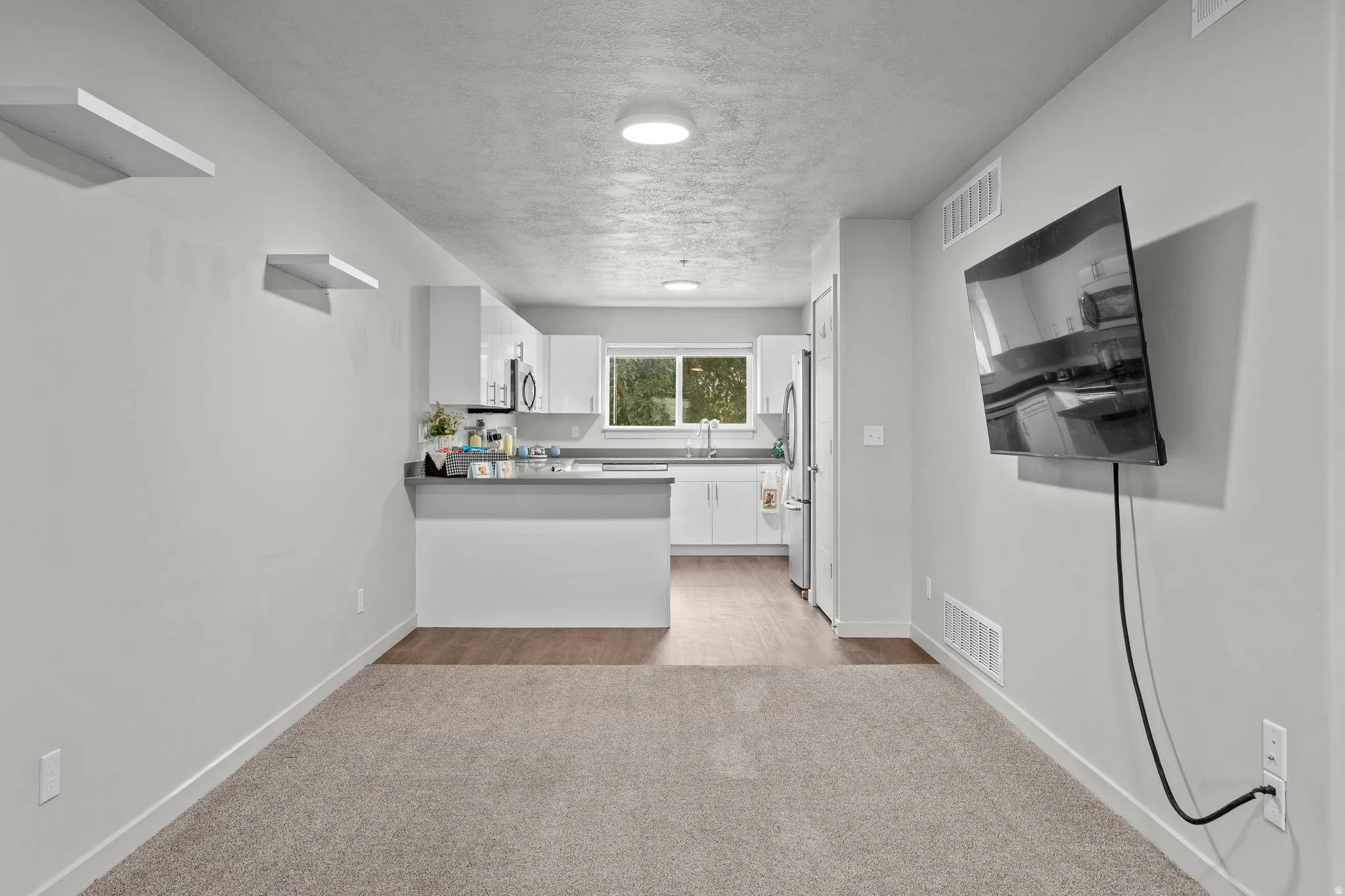 Open concept living area featuring neutral carpeting, recessed ceiling lighting, and a wall-mounted flat-screen television