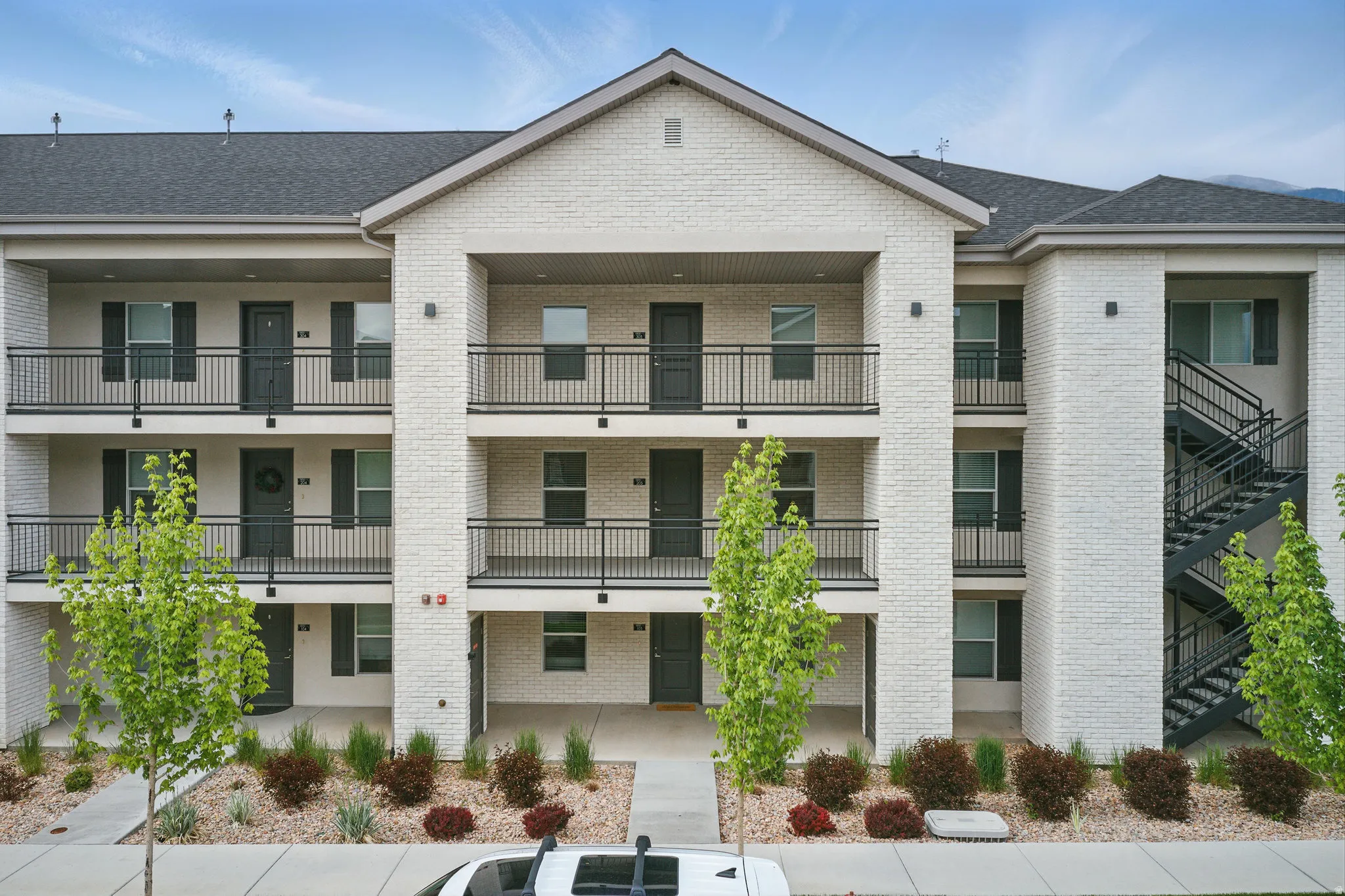 Modern multi-unit residential building featuring clean white brick exterior, multiple covered balconies with metal railings across three stories, and contemporary architectural lines