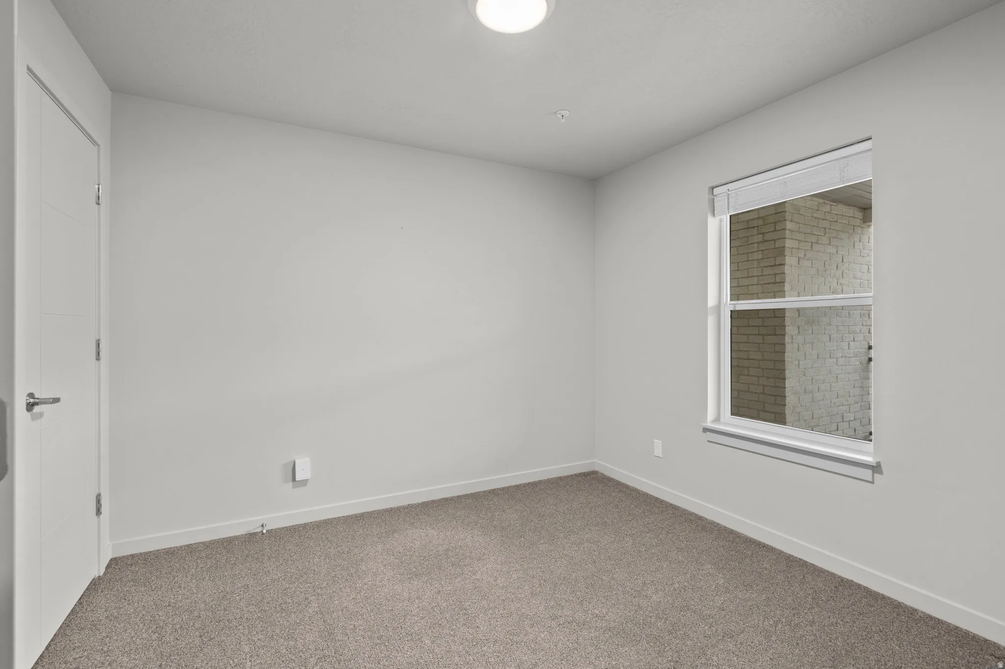 Bright secondary bedroom featuring neutral wall finishes, plush carpeting, a large double-hung window with integrated blinds, and a white six-panel entry door
