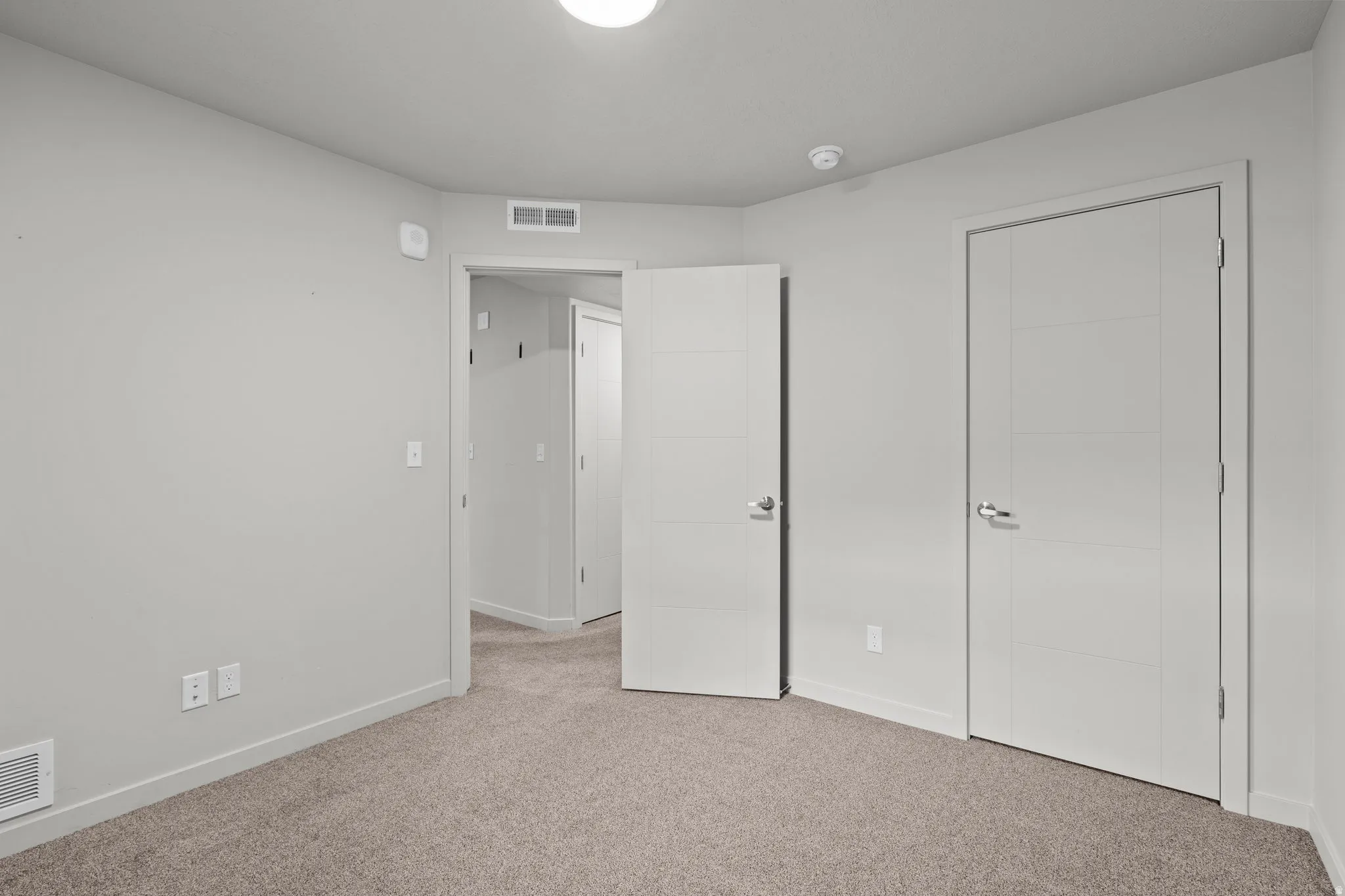 Spacious bedroom featuring neutral carpeting, double closet doors with chrome hardware, and abundant natural light from recessed ceiling fixtures