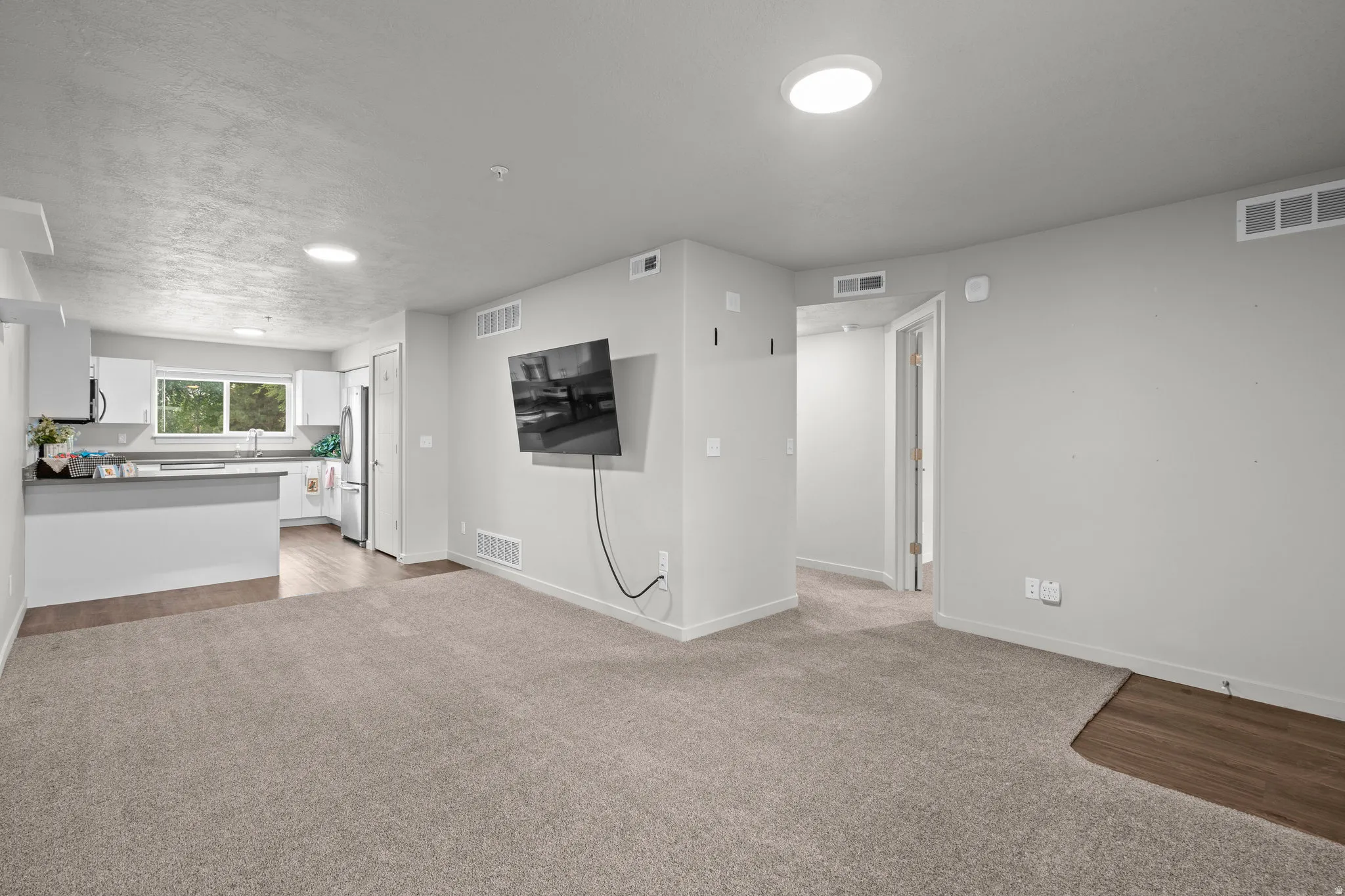 Open concept living space featuring neutral carpeting throughout, recessed ceiling lighting, and a wall-mounted flat-screen television