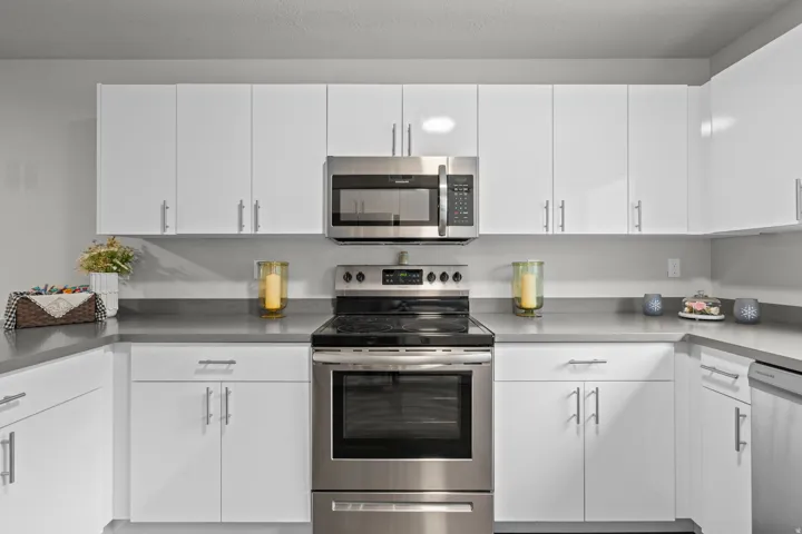 Modern kitchen featuring crisp white cabinetry with chrome hardware, stainless steel appliances including a gas range with convection oven and over-the-range microwave, gray quartz countertops, and a coordinating gray tile backsplash