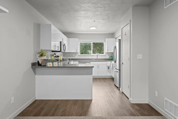 Open-concept kitchen and dining area featuring white cabinetry with a gray quartz countertop island, stainless steel appliances, wood-finish flooring throughout, and abundant natural light from large windows