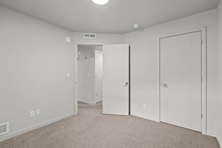 Spacious bedroom featuring neutral carpeting, double closet doors with chrome hardware, and abundant natural light from recessed ceiling fixtures