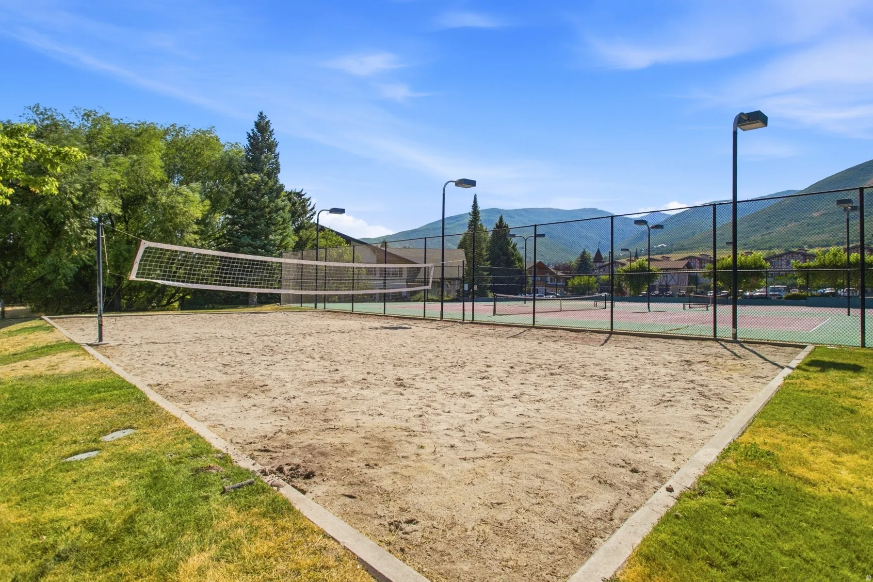 Sand volleyball court featuring a net, concrete border, and perimeter lighting
