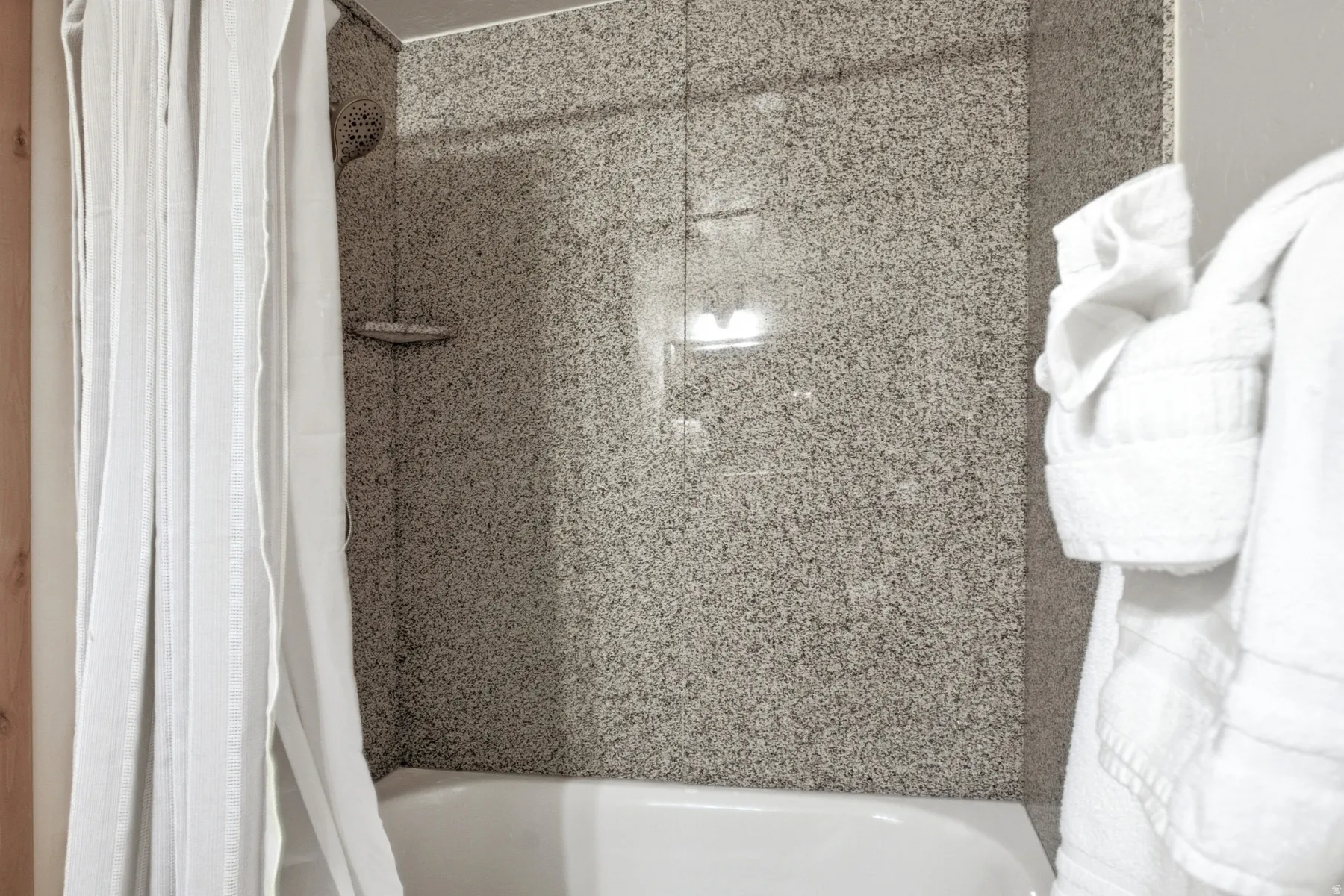 Bathtub with a speckled shower surround and a wall-mounted showerhead