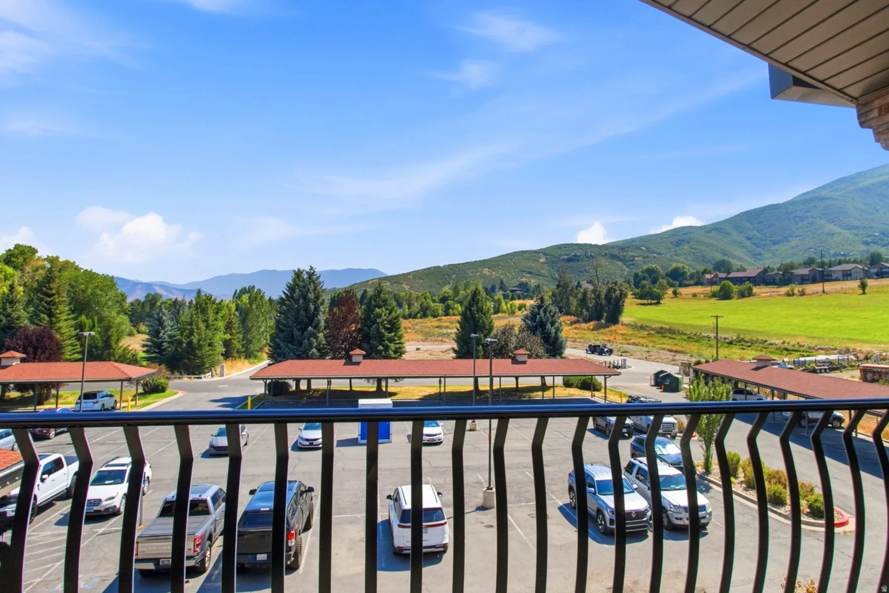 Expansive balcony with black metal railings overlooking manicured grounds, mature landscaping, and rolling mountain vistas