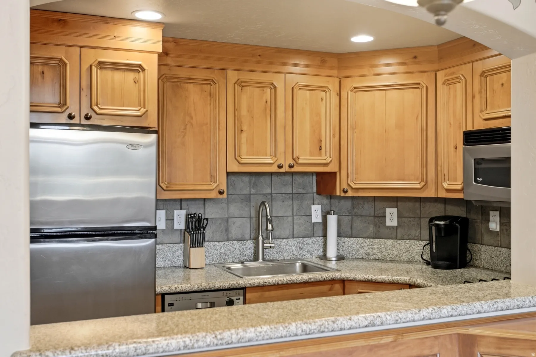Kitchen with wood-finish cabinetry, granite-style countertops, and stainless-steel appliances including a refrigerator, microwave, and dishwasher