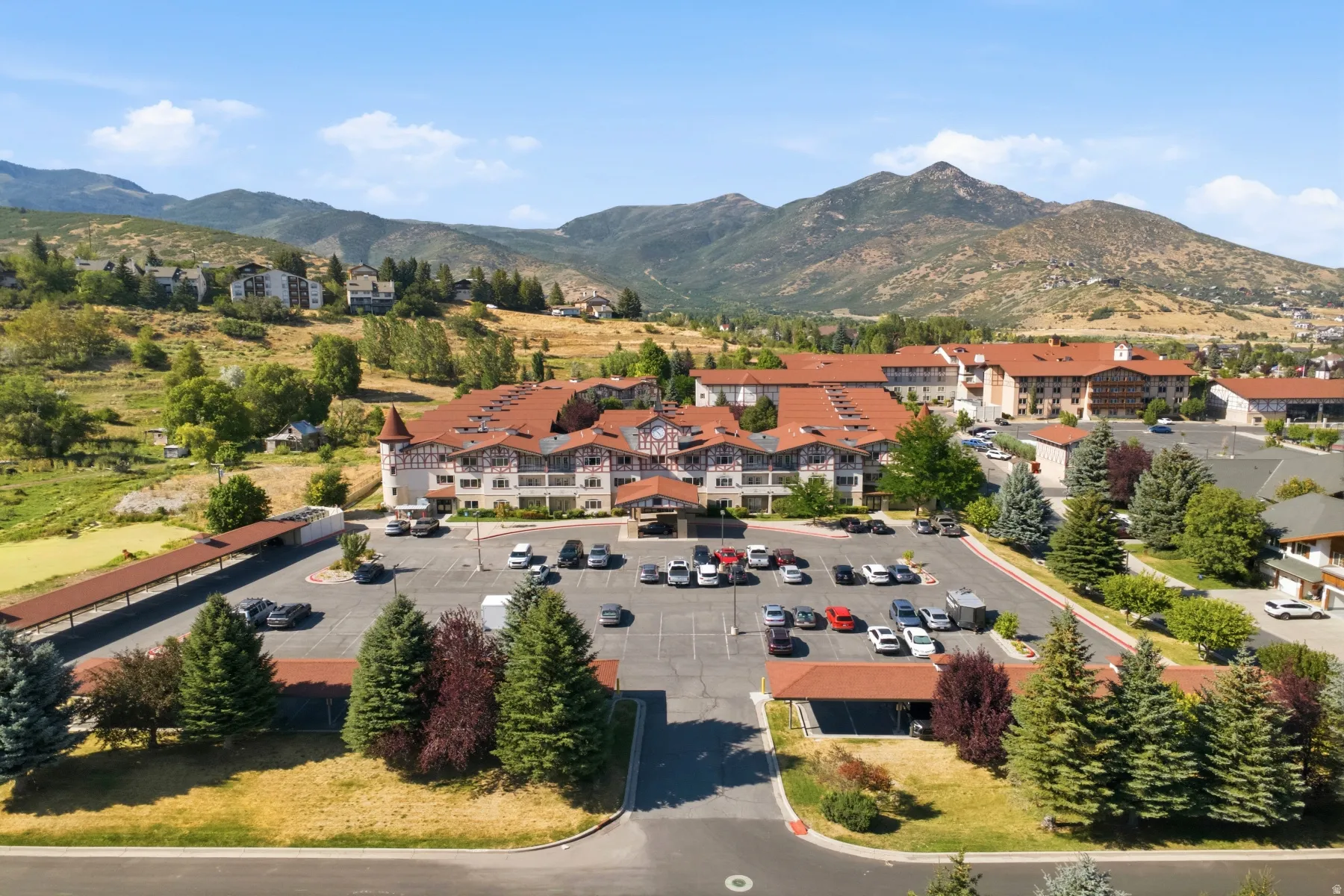 Impressive multi-unit residential complex featuring a substantial asphalt parking area with designated spaces, terracotta tile roofing, and a well-appointed facade with multiple residential wings