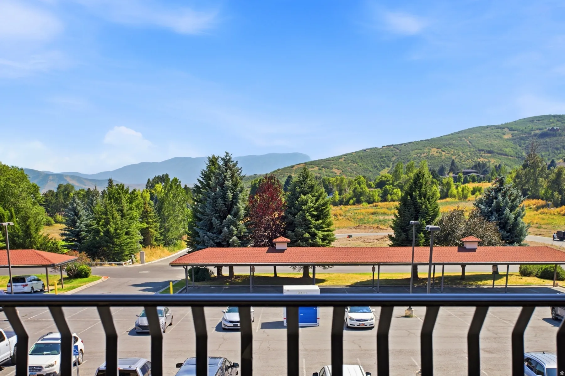 Expansive mountain scenery with established evergreen trees, a clear blue sky, and dedicated covered parking structures