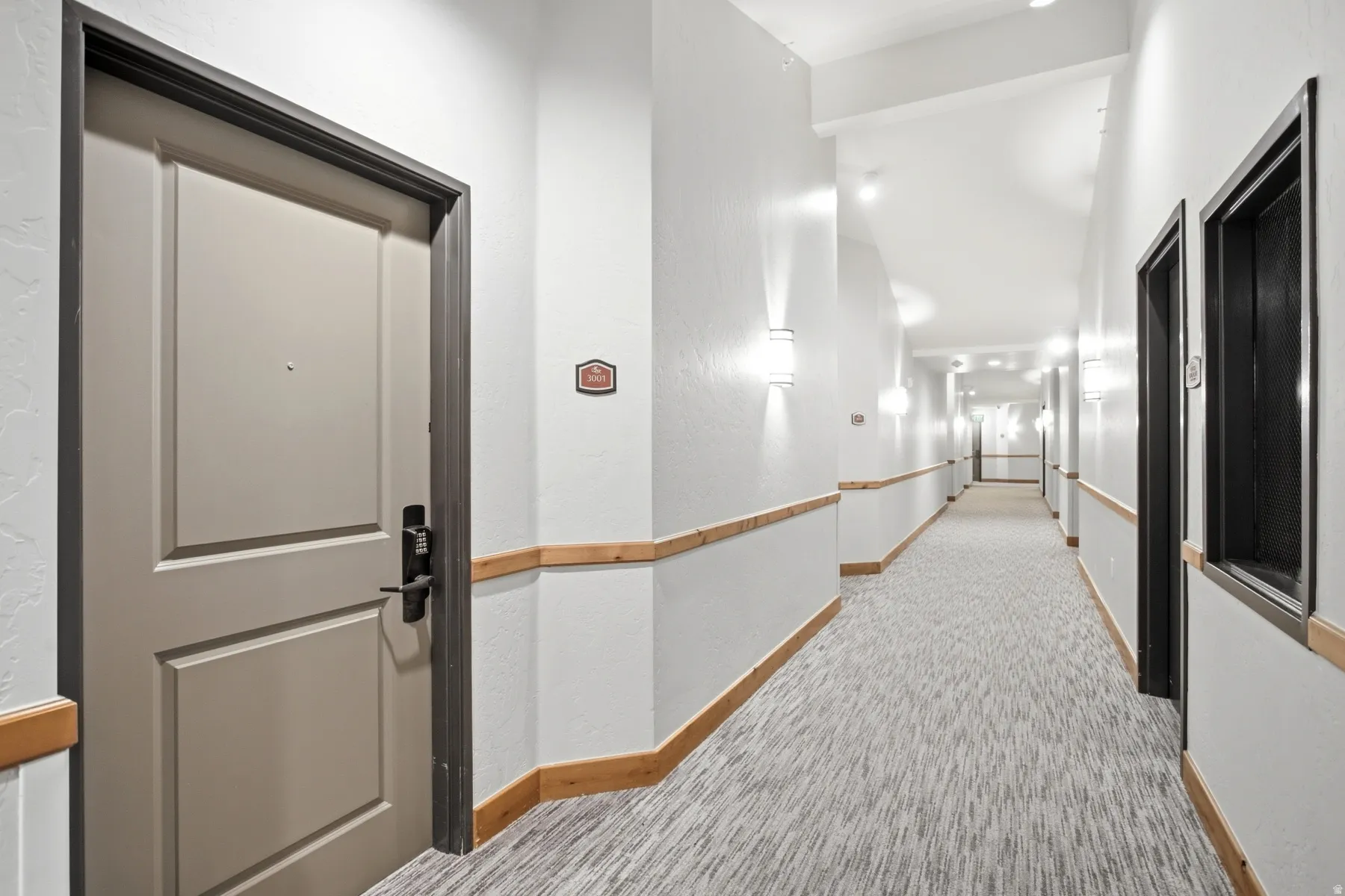 Well-appointed hallway featuring clean white walls, recessed ceiling lighting, and a continuous wood-finish handrail