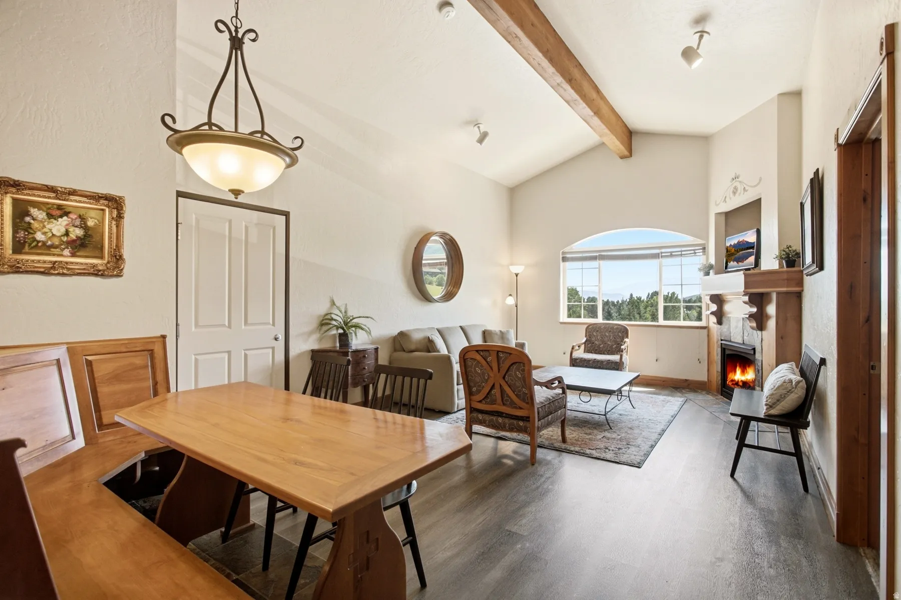 Vaulted ceilings with exposed wood beams, a stone-surround fireplace with a wood mantle, and a large arched window