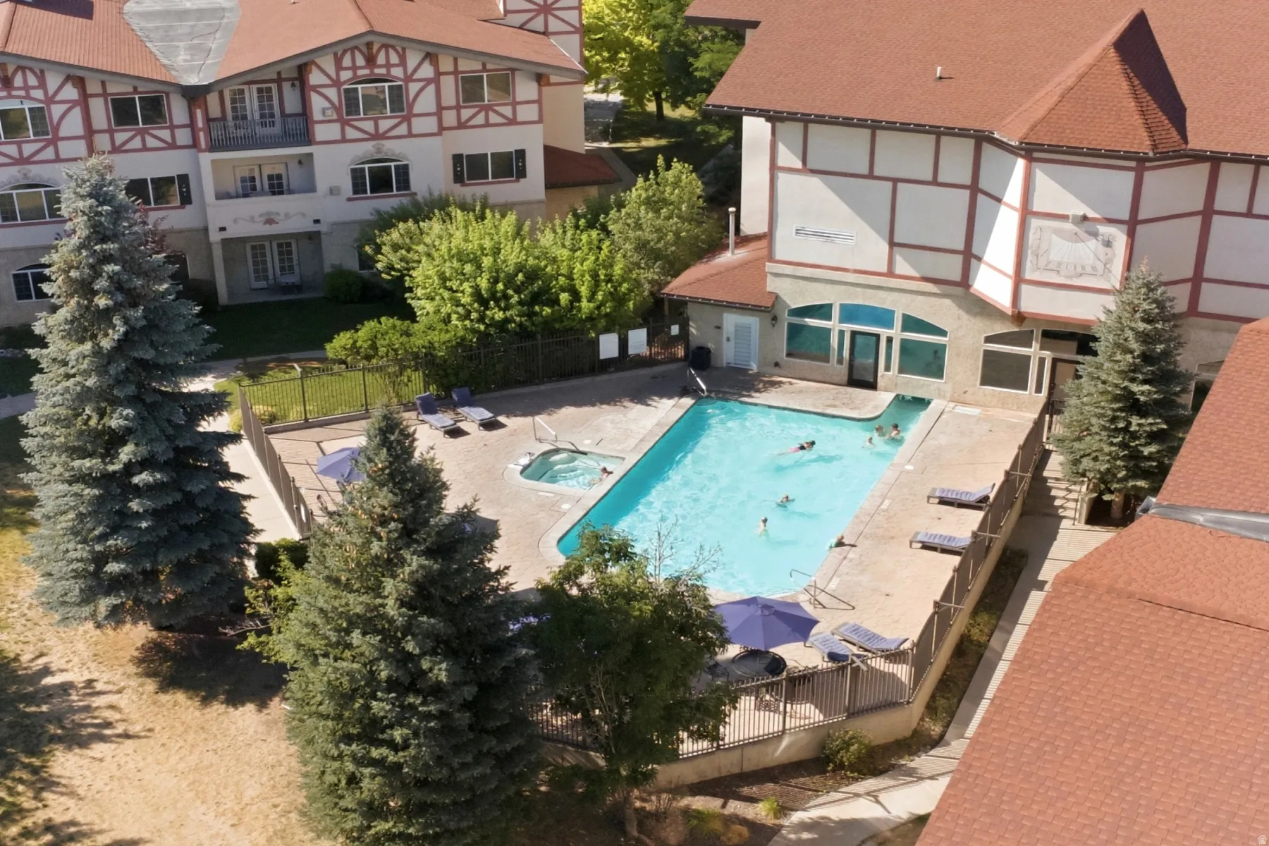 Outdoor pool and hot tub area featuring a fenced perimeter, expansive concrete decking, and mature evergreen trees