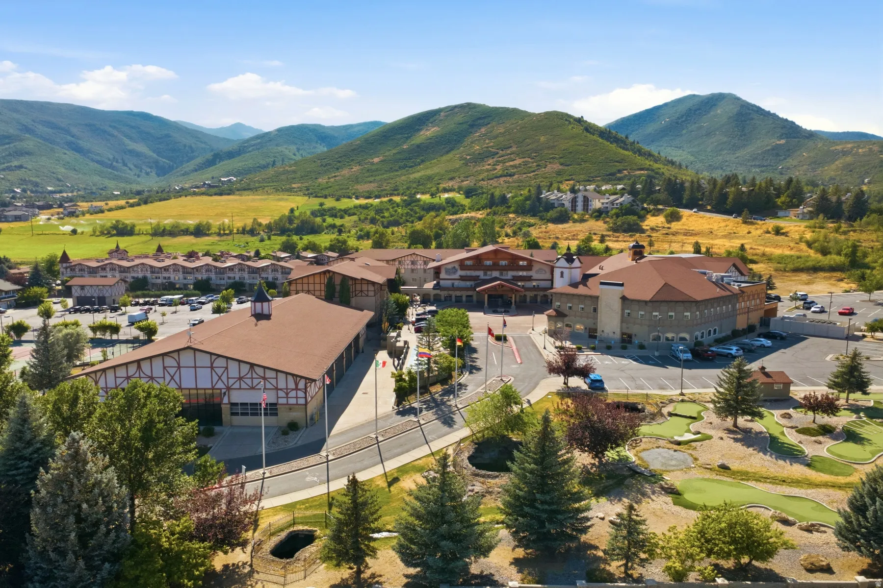 Modern commercial or mixed-use property featuring expansive copper-toned metal-clad structures with pitched rooflines, situated on manicured grounds with mature coniferous landscaping