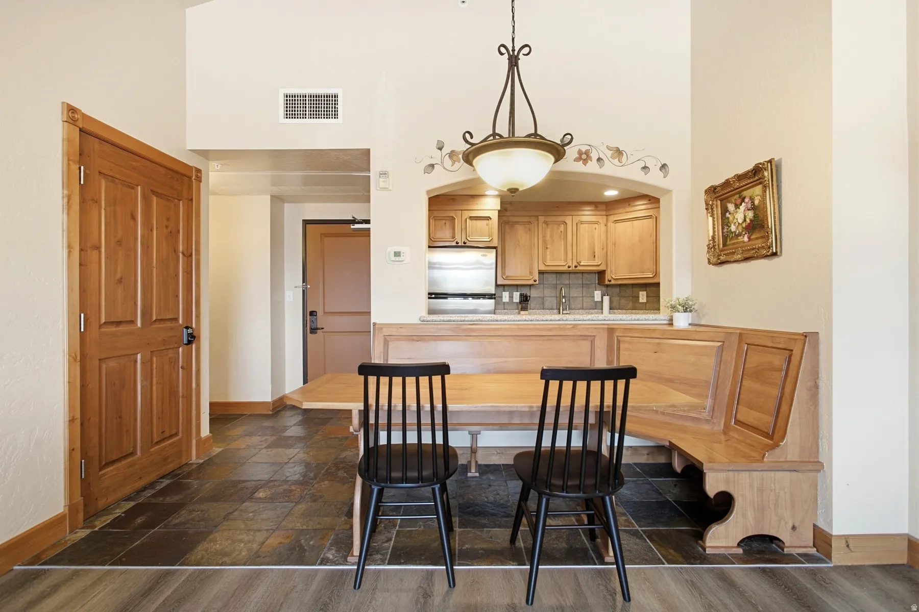 Open-concept dining and kitchen area featuring a wood-finish table with built-in bench seating, black spindle-back chairs, and warm wood cabinetry with a center island
