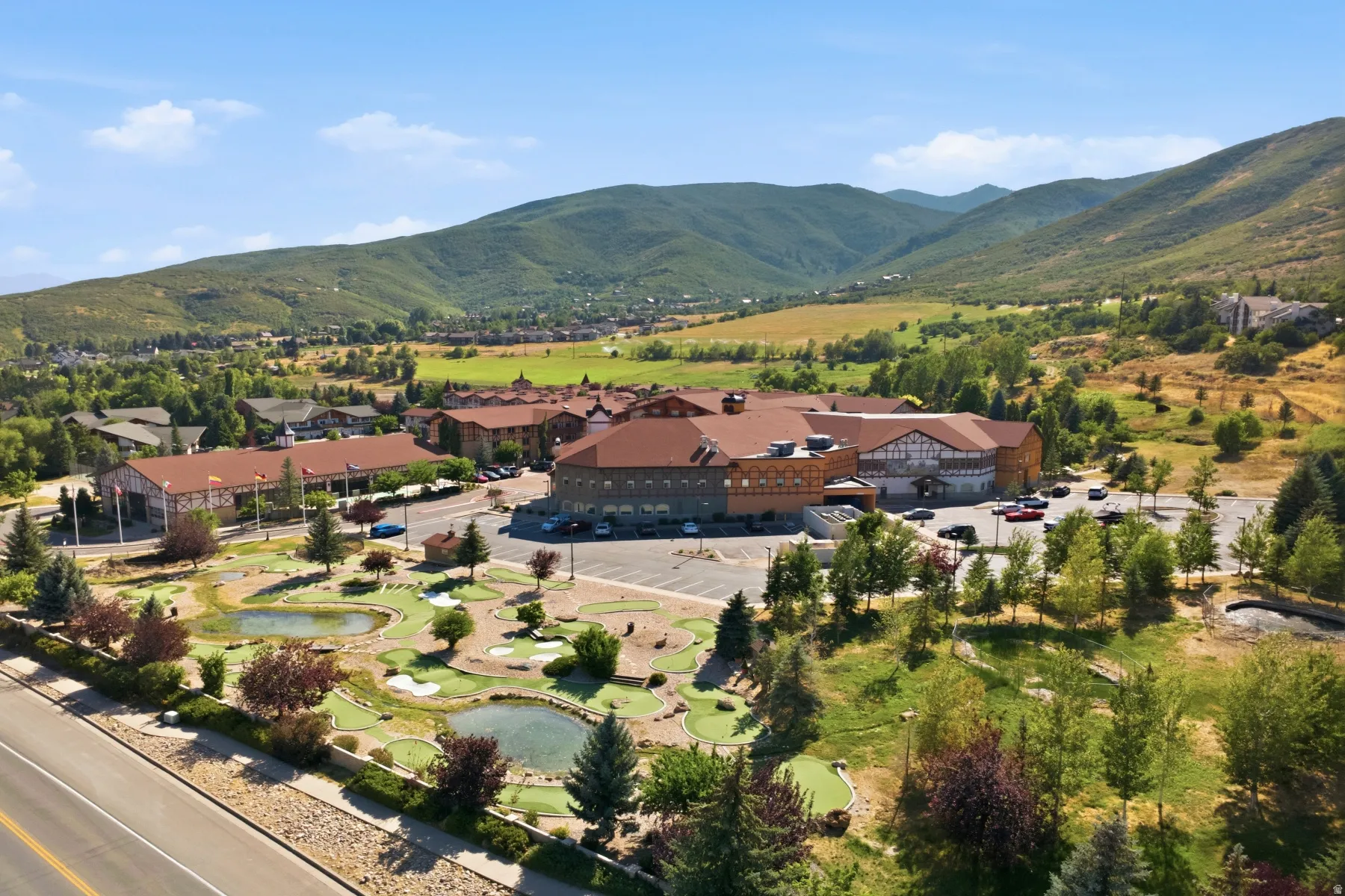 Expansive property with a multi-story building featuring a brown roof and stone facade, surrounded by lush green landscapes