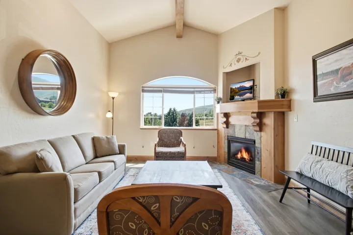 Bright, open living room featuring vaulted ceilings, large multi-pane windows with expansive natural light, and wood-finish flooring throughout