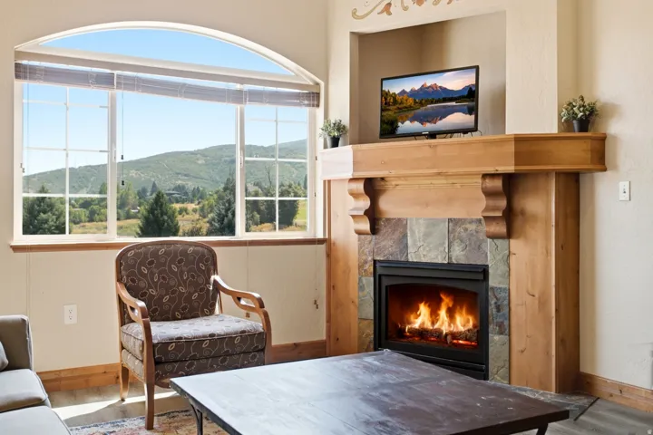 Arched picture window with mountain scenery, featuring a stone-faced fireplace with a wood mantle