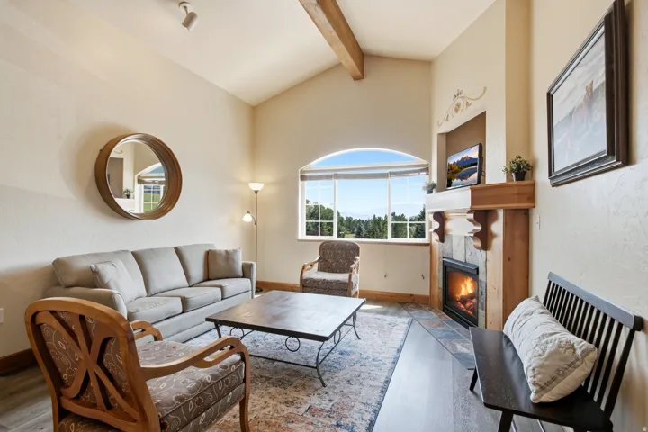 Living area featuring a vaulted ceiling with exposed wood beams, a fireplace with a stone surround and wood mantel, and large arched windows