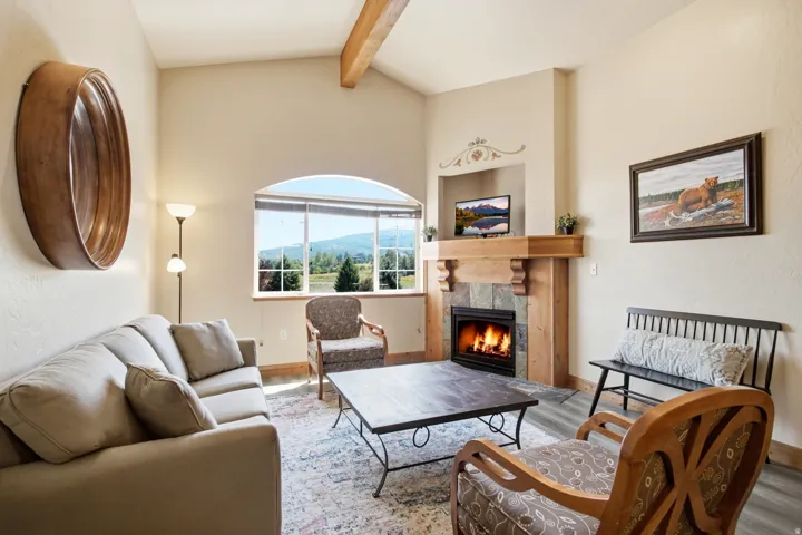 Arched window providing natural light, vaulted ceiling with exposed wood beam, natural stone fireplace with wood mantel, built-in media niche, and wood-finish flooring