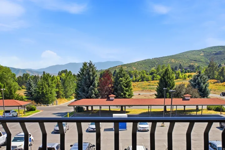 Expansive mountain scenery with established evergreen trees, a clear blue sky, and dedicated covered parking structures
