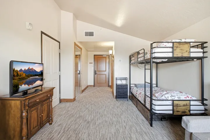 Spacious room featuring bunk beds with integrated storage, neutral-toned patterned carpeting, and a wood-finish media console