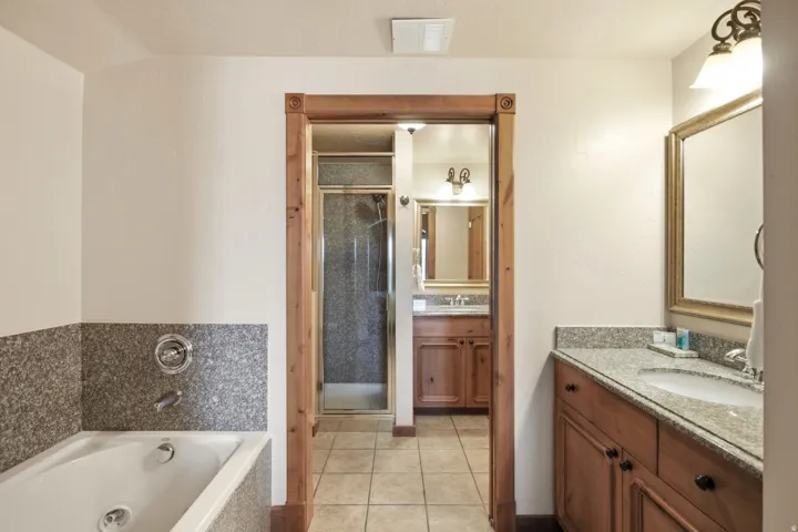 Bathroom featuring a built-in jetted tub, granite-look surround, wood-trimmed doorway, tile flooring, and a vanity with granite-look countertop and wood cabinetry