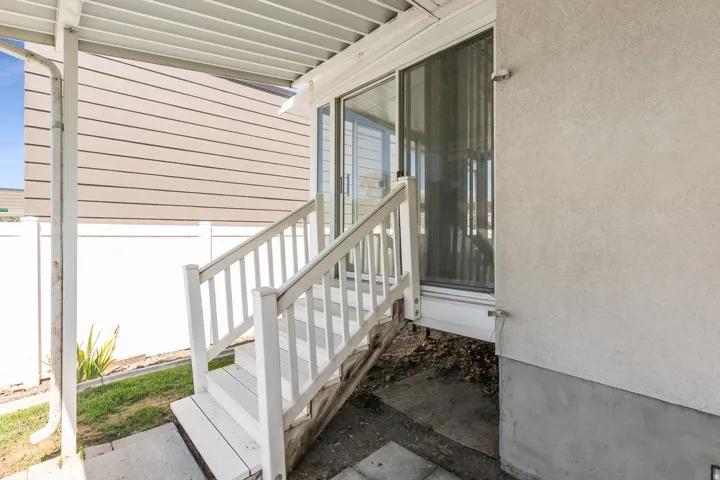 Rear Covered Entry featuring a white aluminum railing, concrete foundation, and direct access to the home via glass sliding doors.  Enters into Enclosed Porch