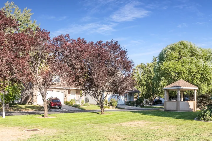 Expansive green space featuring a built-in gazebo with a shingled roof, mature trees, and manicured landscaping